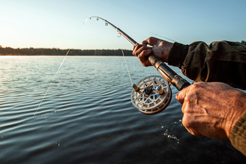 Hands of a man in a Urp plan hold a fishing rod, a fisherman catches fish at dawn. Fishing hobby...