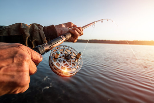Hands of a man in a Urp plan hold a fishing rod, a fisherman catches fish at dawn. Fishing hobby vacation concept. Copy space.
