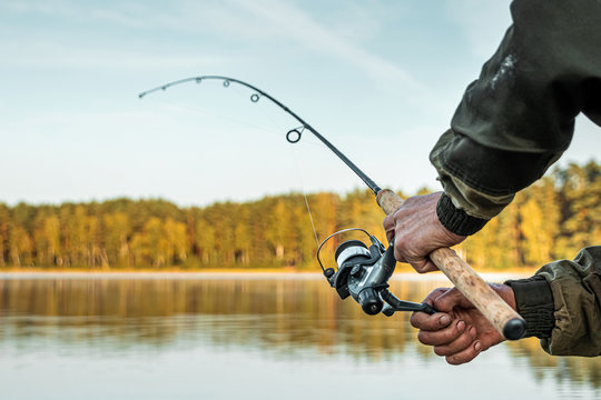 Hands of a man in a Urp plan hold a fishing rod, a fisherman catches fish at dawn. Fishing hobby vacation concept. Copy space.