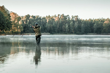 Fototapeta na wymiar A male fisherman on the lake is standing in the water and fishing for a fishing rod. Fishing hobby vacation concept. Copy space.