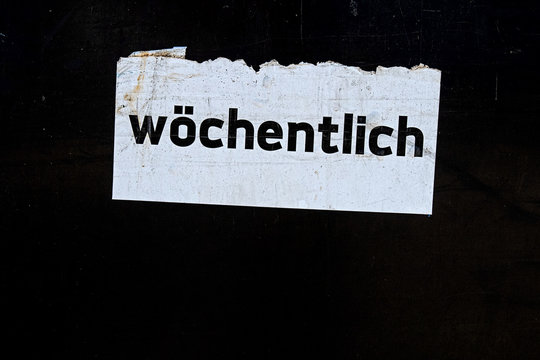 the word "w&ouml;chentlich" written in German language on a white sign on black background,  translated "weekly"