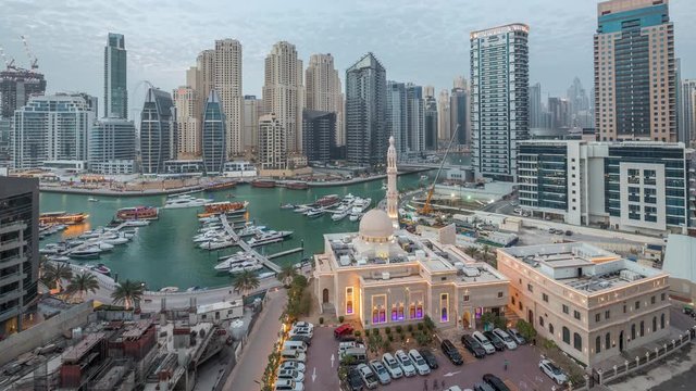 Yachts in Dubai Marina flanked by the Al Rahim Mosque and residential towers and skyscrapers aerial day to night transition timelapse. Modern high rise skyline with boats and wooden dhows