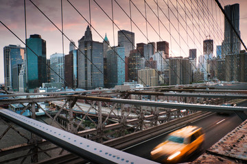 A yellow cab riding across the Brooklyn Bridge at sunset with New York city skyline in the...