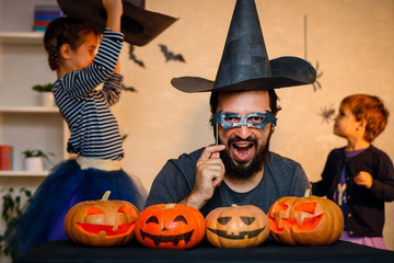 Fototapeta premium Happy family: father, brother and sister celebrate Halloween. Cheerful children in carnival costumes indoors. Cheerful children and parents play with pumpkins and black witch hats