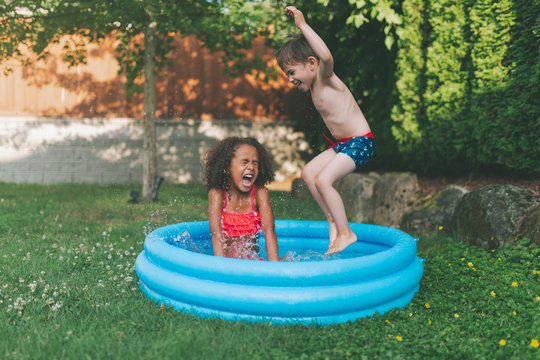 Two children playing together in a backyard swim pool. 