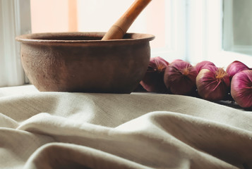 rustic flat lay, clay mortar with wooden pestle for grinding spices on linen background and string of onions on windowsill