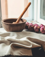 rustic flat lay, clay mortar with wooden pestle for grinding spices on linen background and string of onions on windowsill
