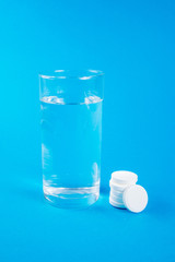 Clear glass of water and soluble effervescent tablets isolated on blue background. The concept of treatment and prevention of viral diseases. Help with depression and insomnia.To drink liquid medicine