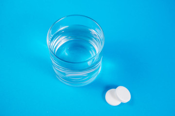 Clear glass of water and soluble effervescent tablets isolated on blue background. The concept of treatment and prevention of viral diseases. Help with depression and insomnia.To drink liquid medicine