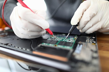 Male hands in white protective glove hold contact probe an electronic circuit tester. Laptop repair...