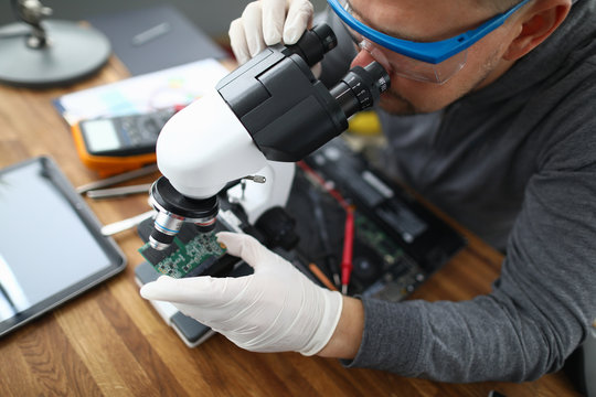Male worker pc repair service in white protective gloves use microscope and holding micro chip. Hardware soft testing concept