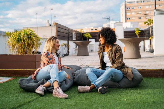 Multicultural women talking sitting on cushions on a terrace