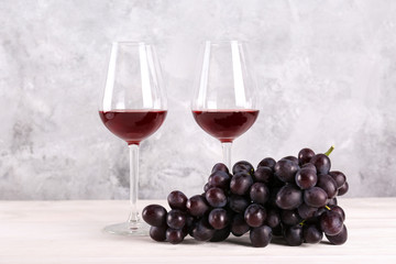 Two glasses of vintage red wine and bunch of grapes on wooden table, grunged concrete wall...