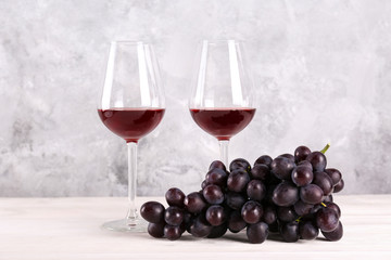 Two glasses of vintage red wine and bunch of grapes on wooden table, grunged concrete wall background. Expensive bottle of cabernet sauvignon concept. Copy space,