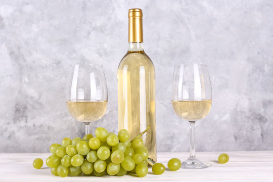 Vintage bottle of white wine without label, two glasses and bunch of grapes on wooden table, lofty grunged concrete wall background. Expensive bottle of chardonnay concept. concept. Copy space,