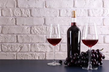 Fototapeta na wymiar Vintage bottle of red wine without label, two glasses and bunch of grapes on wooden table, lofty white brick wall background. Expensive bottle of cabernet sauvignon concept. Copy space,