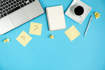 Asking, Decisions. Question mark on sticky notes, notebook, cup coffee, laptop and pen on blue background. FAQ concept. Working with clients. Troubles in work. Flat lay, top view, copy space