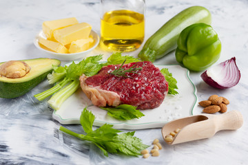 Raw steak on the plate.  Beef, vegetables, nuts and oil on marble background.  Keto diet concept