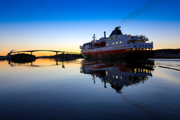Coastal ships Ms Nordlys depart from Bronnoysund harbor in sunset, Northern Norway