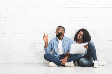 Young couple with laptop pointing at empty space