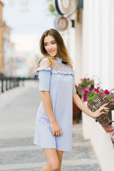 A young beautiful girl in a blue dress walks around the city, smiling, happy and enjoying life