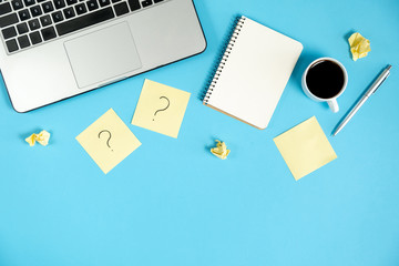 Question mark on sticky notes, notebook, cup coffee, laptop and pen on blue background. FAQ...