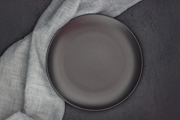 Black plate, cutlery and napkin on stone table top view. Table setting.