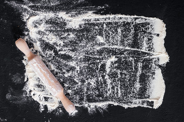 Rolling pin and white flour on a dark background. Free space for text . Top view.