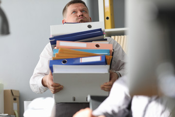 Male businessman carries a bunch of folders and documents in hand against office background. Lot of...