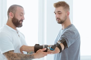 Tattooed physiotherapist who puts an orthosis on the hand of a young patient after an accident