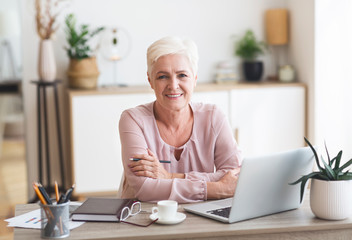 Smiling senior business woman working with laptop at home