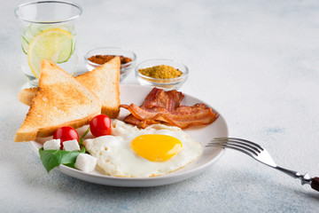Fried egg with bacon, toast, tomatoes and a glass of mineral water with lemon and cucumber on a white background. English breakfast. with copy space for your text