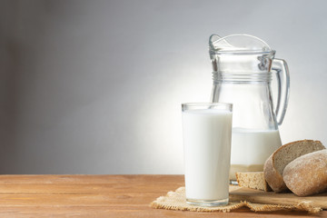 Glass cup and jug of milk, sliced fresh bread, on a wooden table