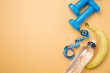 Blue hand dumbbells, a bottle of water, banana, on an orange background