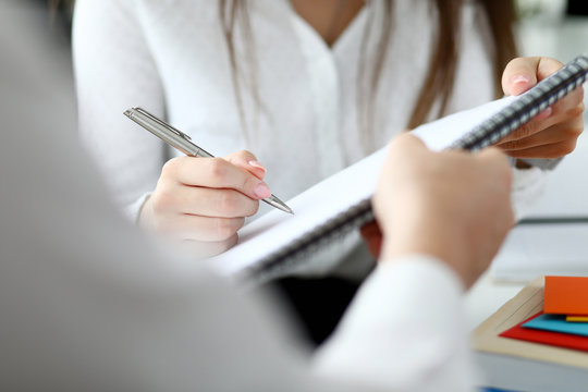 Close-up of people sitting in office and writing something in important document with tender female hands. Smart businessman holding paper folder. Blurred background