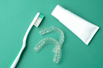 Toothbrush, plastic mouthpiece and tube of toothpaste on a green background, close-up