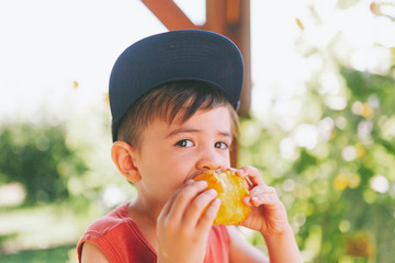 A little boy eating a juicy peach in summer.