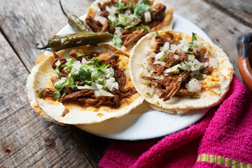 Mexican birria tacos with onion and cilantro on wooden background