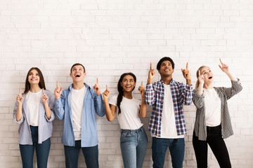 Teen friends pointing up on free space over white wall