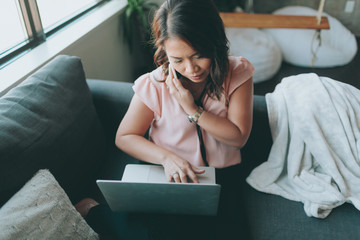 A professional asian business woman talking on the phone and using a lap top computer.