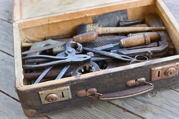 A suitcase with old hand tools on a wooden background. Focus on the suitcase