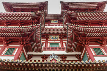 Fototapeta na wymiar Singapore - March 22, 2019: Chinatown. Fish eye view on pagoda-like structure of main entrance maroon-red facade of Buddha Tooth Relic Temple.
