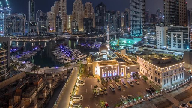 Yachts in Dubai Marina flanked by the Al Rahim Mosque and residential towers and skyscrapers aerial night to day transition timelapse. Modern high rise skyline with boats and wooden dhows