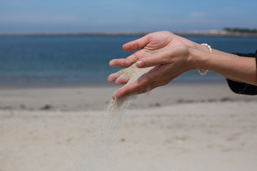 Fototapeta na wymiar Closeup sand pours through fingers against the sea.