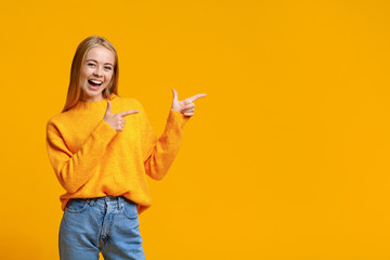 Cheerful teenage girl pointing at copy space on orange background