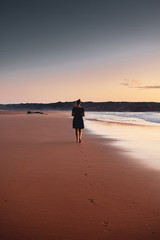Naklejka premium Silhouette of a girl in colorful sunset gradient at a peaceful beach on a tropical beach. Praia da Bordeira at the Algarve Coast in Portugal, Atlantic Ocean