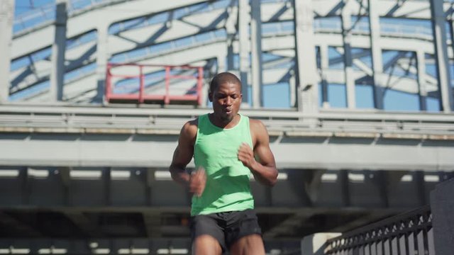 Young African athlete breathing actively while practicing backward running drill exercise on urban bridge