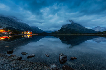 Beautiful View of the reflection in the water with the Cloudy Morning Sunrise in the American Rockies. Taken in Swiftcurrent Lake, Glacier National Park, Montana, United States.