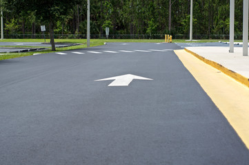 Looking down the length of an empty parking lot with arrow pointing in direction to go, with crosswalk and sidewalk.