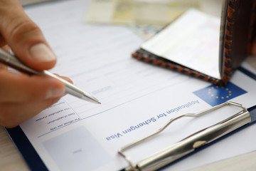 Male hand hold silver pen with passport. Filling Schengen apllication form concept